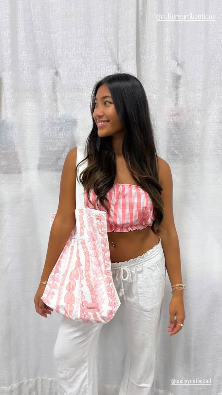 Woman wearing a Culture Girl pink Palaka print top and white pants against a light gray curtain background