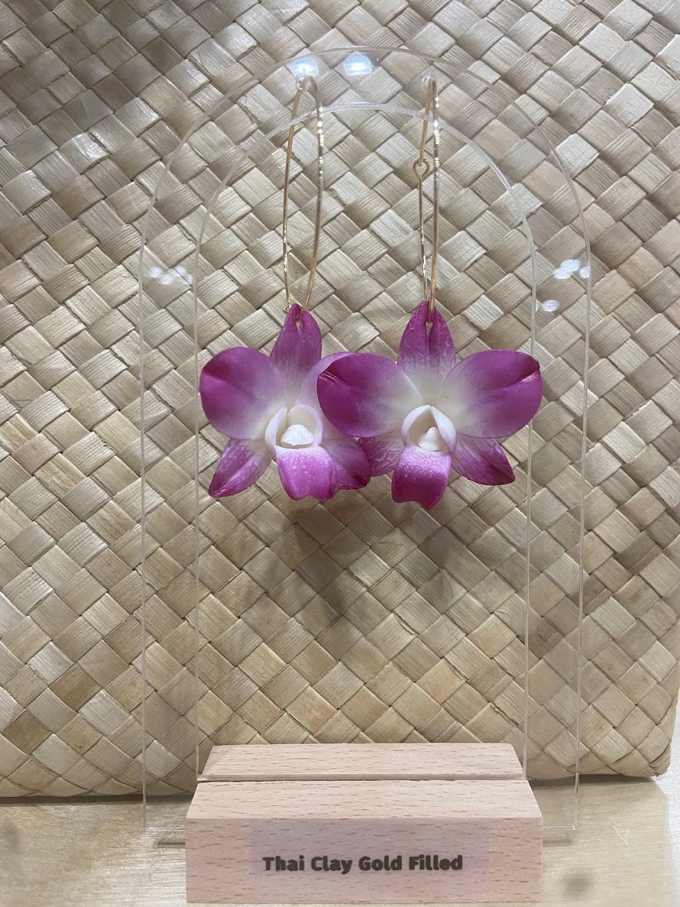 Purple thai handmade clay earrings on a clear stand with 'Thai Clay Gold Filled' label against a textured beige background.