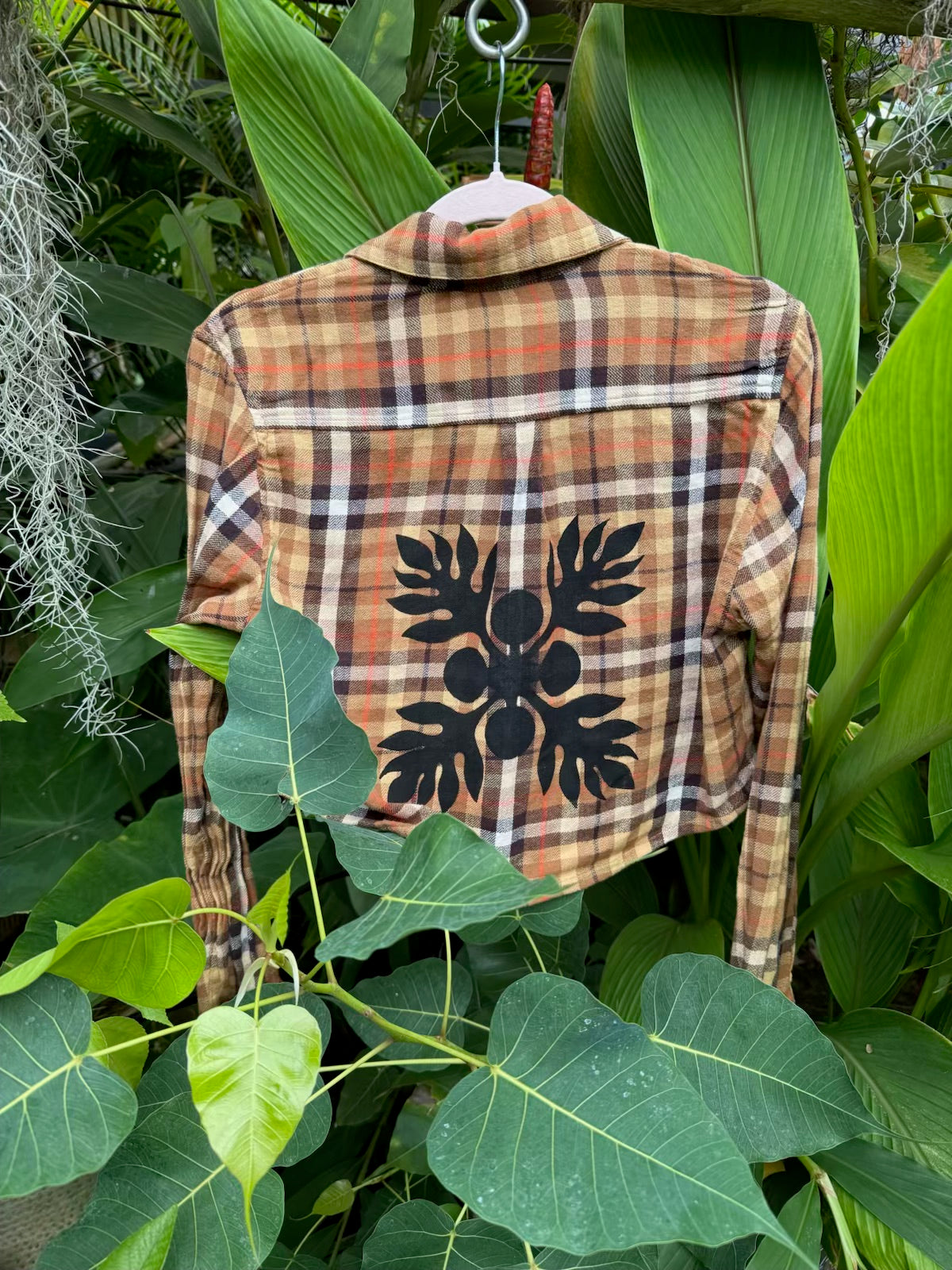 Culture Girl plaid print denim button down jacket with black ulu print design hanging among green leaves