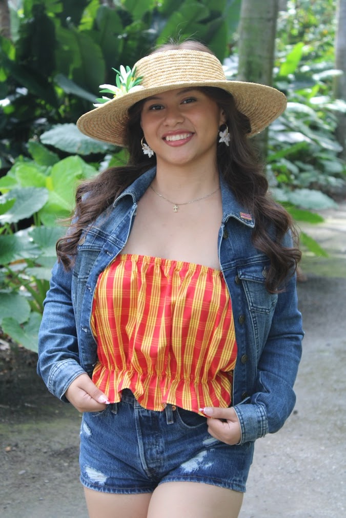 Model wearing hand-painted Hawaiian print design denim jacket and shorts, Palaka print top, handmade Pikake clay hoop earrings and a straw hat, crafted in Hawai‘i by Culture Girl Boutique