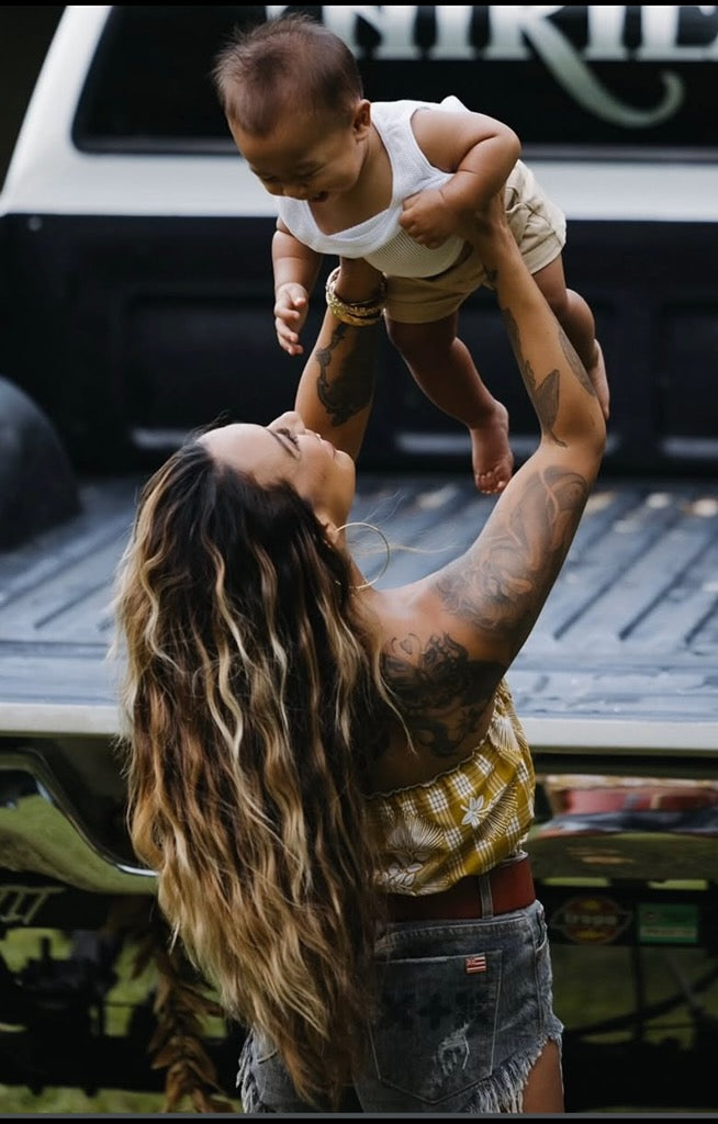 Woman lifting a baby up and wearing Culture Girl Boutique palaka print yellow bandeau
