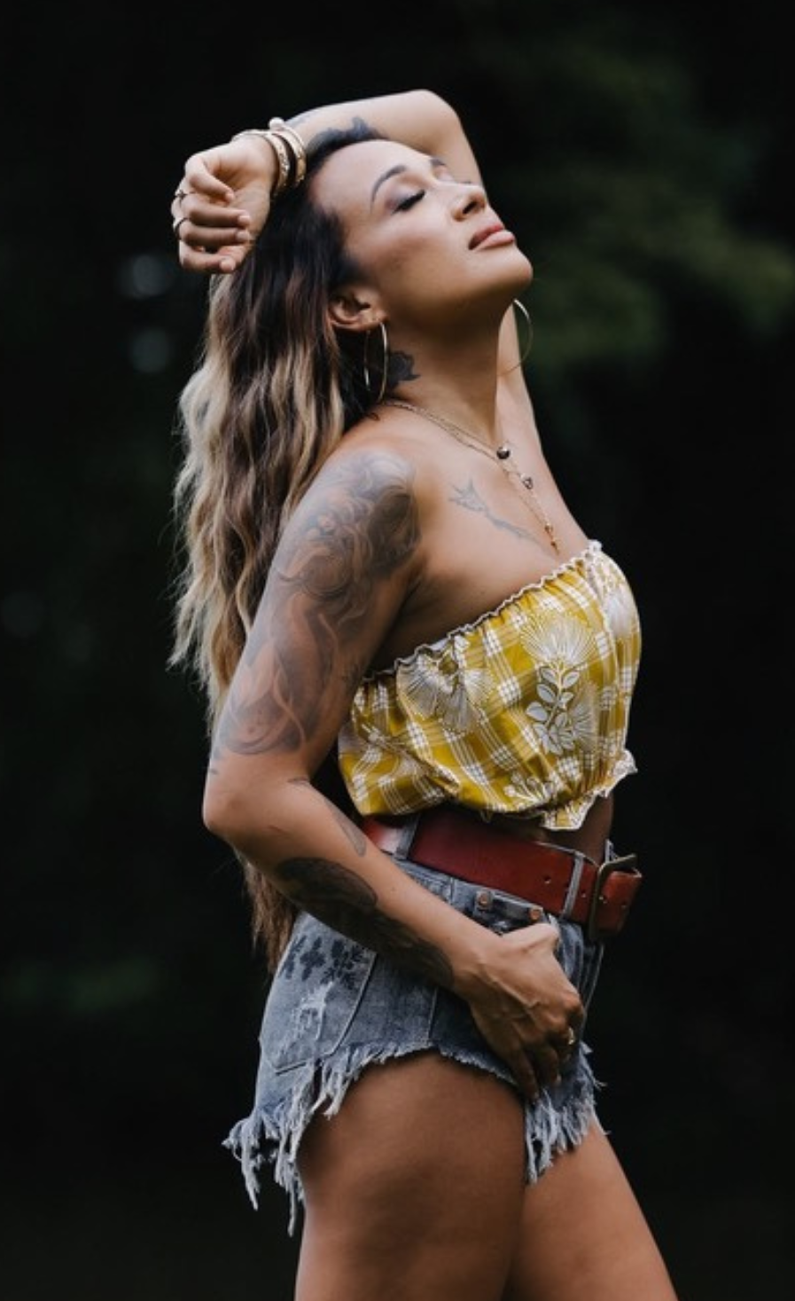 Woman in a yellow palaka print top and denim shorts with tattoos outdoors