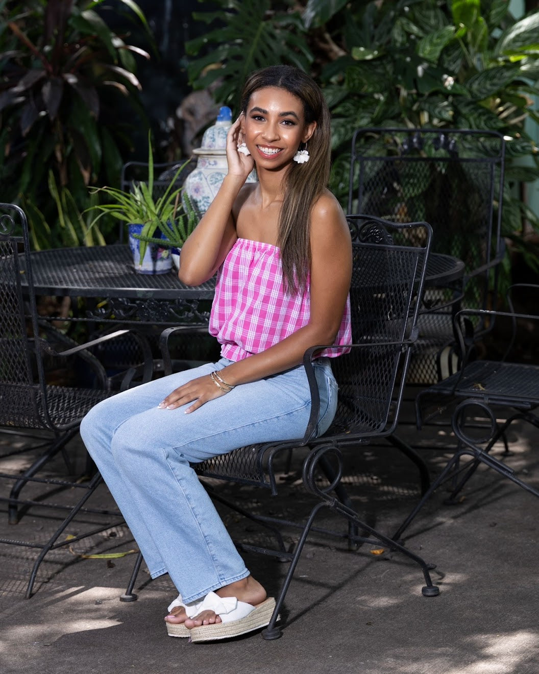 Model sitting outdoors in a Hawaiian Palaka print top, jeans and. handmade Pikake clay hoop earrings, crafted in Hawai‘i by Culture Girl Boutique