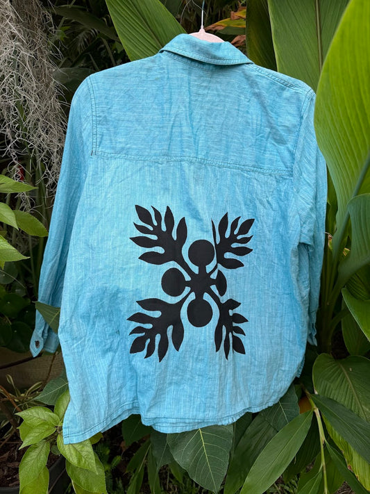 Light blue denim button down jacket with a black Hawaiian Ulu print design on a green leafy background